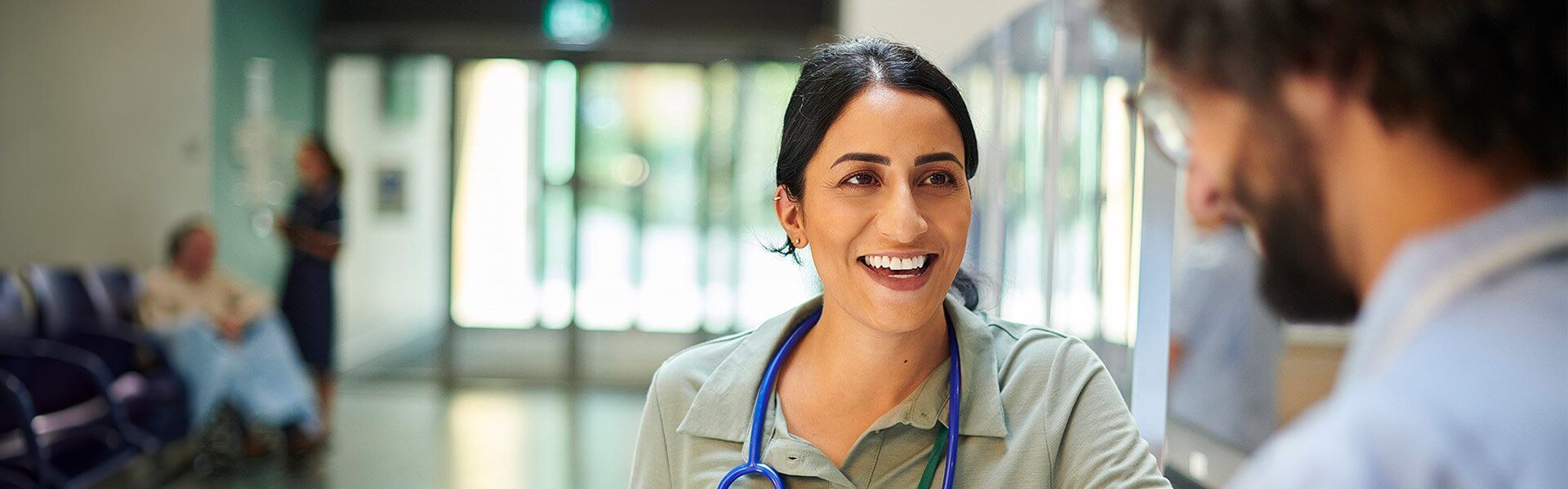 A doctor in a hospital setting speaks to a co-worker, showing an attentive expression during the conversation.